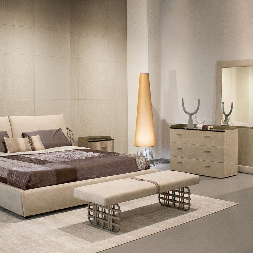 Modern bedroom with beige bed, dresser, and mirror in a neutral-toned room.