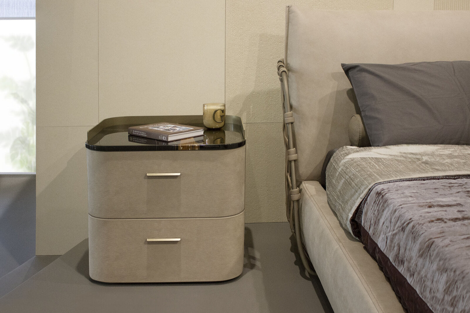 Beige nightstand with glass top next to a bed in a bedroom setting