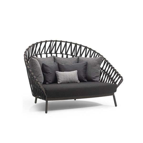 A daybed with a cocooning shape, featuring a black seat cushion with Dryfeel foam padding and a powder-coated aluminum frame. It has a distinctive acrylic fabric band in a weaving pattern.