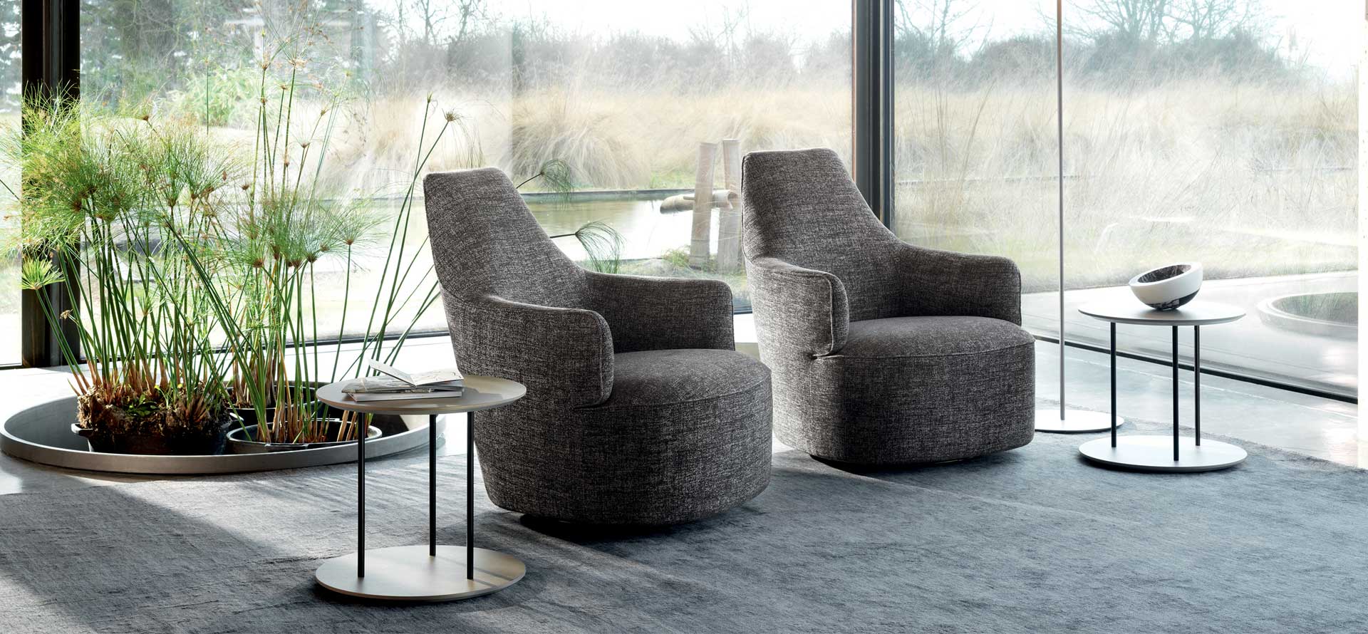 Modern gray armchairs in a stylish room with large windows and decorative plants.
