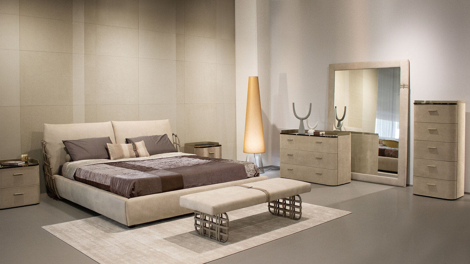 Modern bedroom with beige bed, dresser, and mirror in a neutral-toned room.